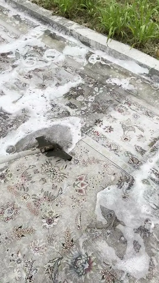 A metal rake pushing soapy water out of a pale floral rug